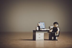 distressed-looking lego person sitting at lego desk with lego computer equipment